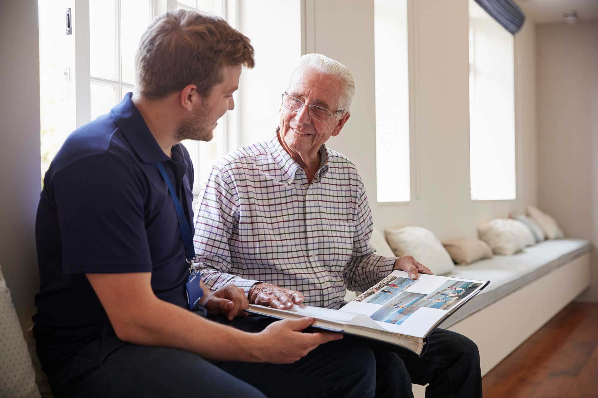 Senior man sitting looking at photo album  with male nurse